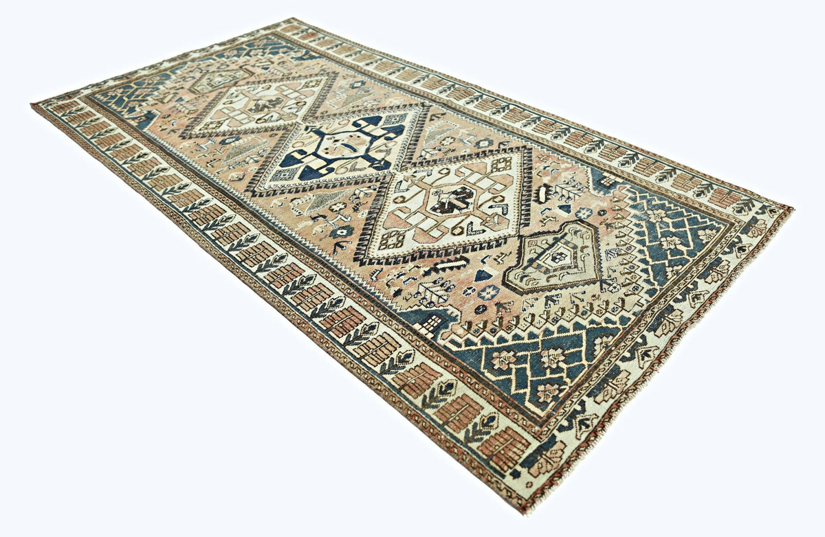A vintage handmade Persian rug featuring geometric diamond patterns in blue and beige tones.