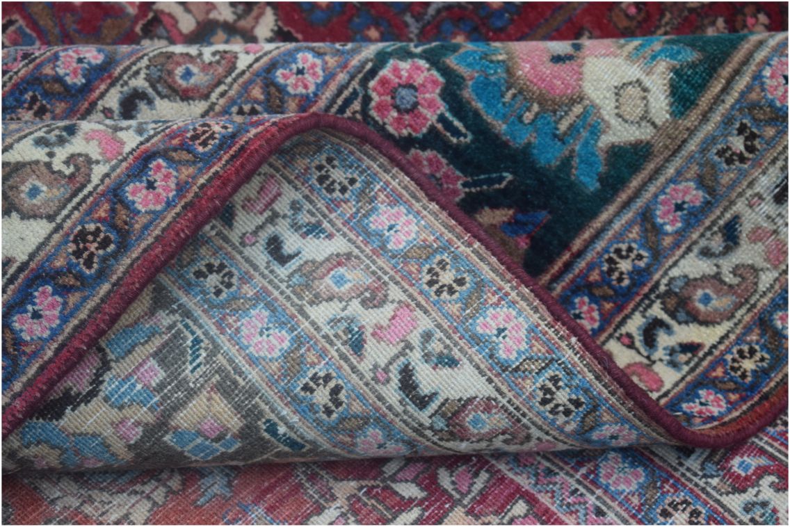 A folded vintage Persian rug featuring intricate floral patterns in red, blue, and cream tones.