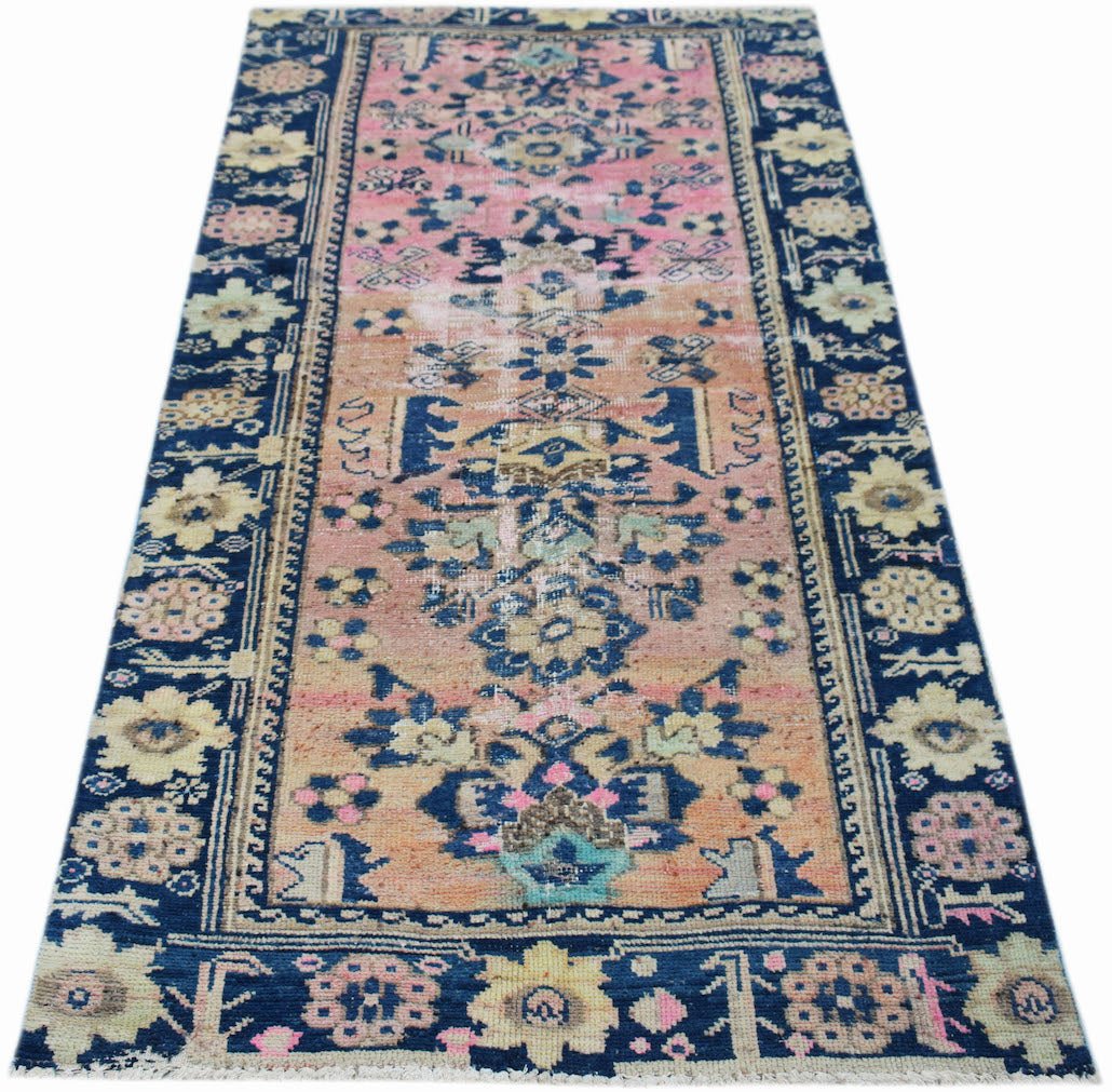 A vintage handwoven Persian runner featuring a floral pattern in faded pink, orange, and blue tones.