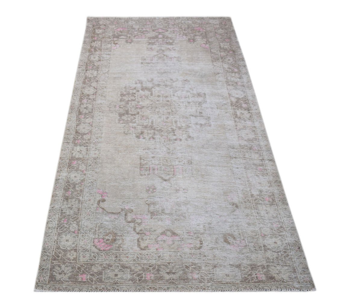 A vintage Persian runner rug featuring a faded beige pattern with subtle pink accents.
