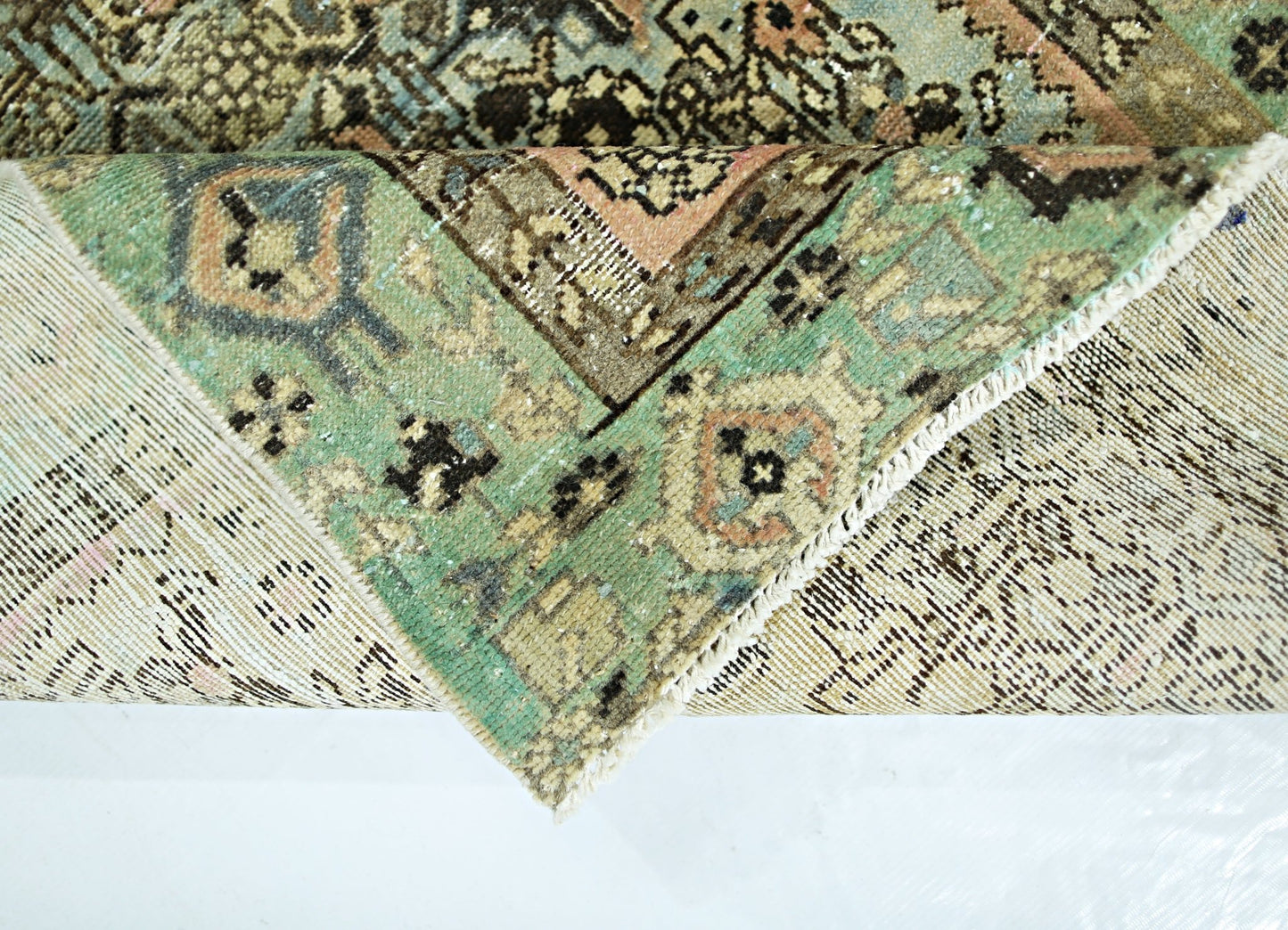 A corner of a vintage Persian runner with a green, pink, and brown geometric pattern.