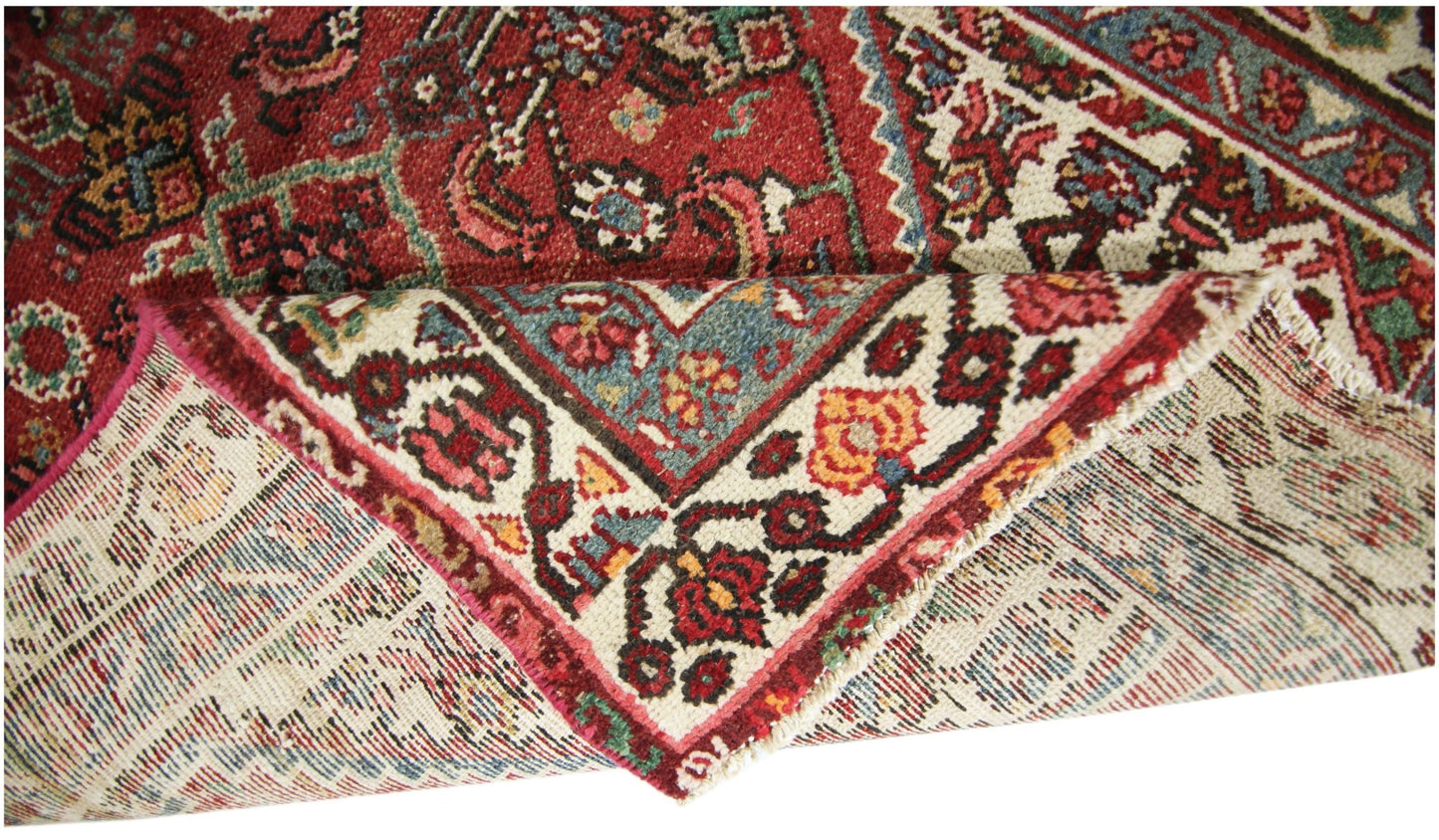 A corner of a vintage Persian runner with a red field and intricate floral patterns.