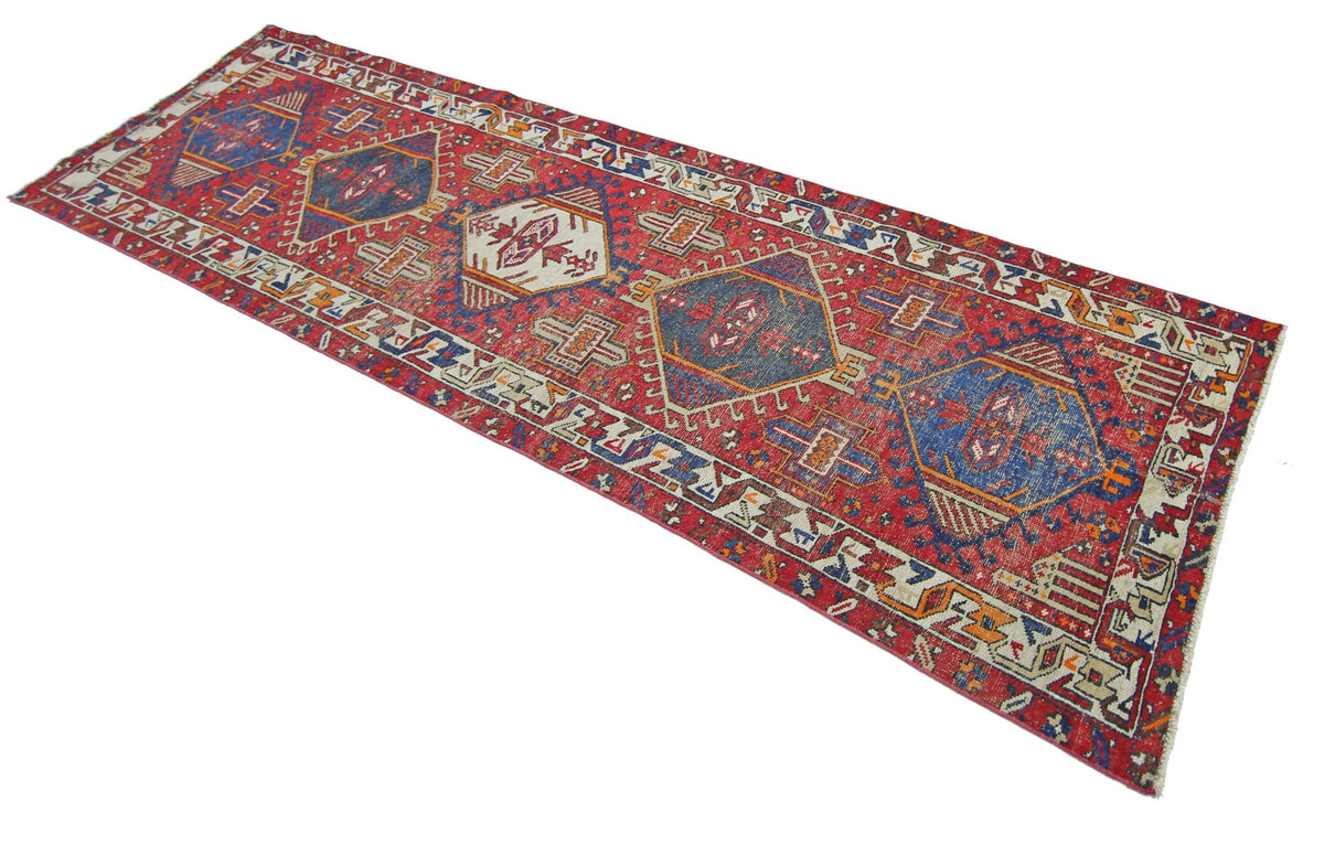 A vintage handmade Persian runner featuring geometric diamond medallions on a red field.