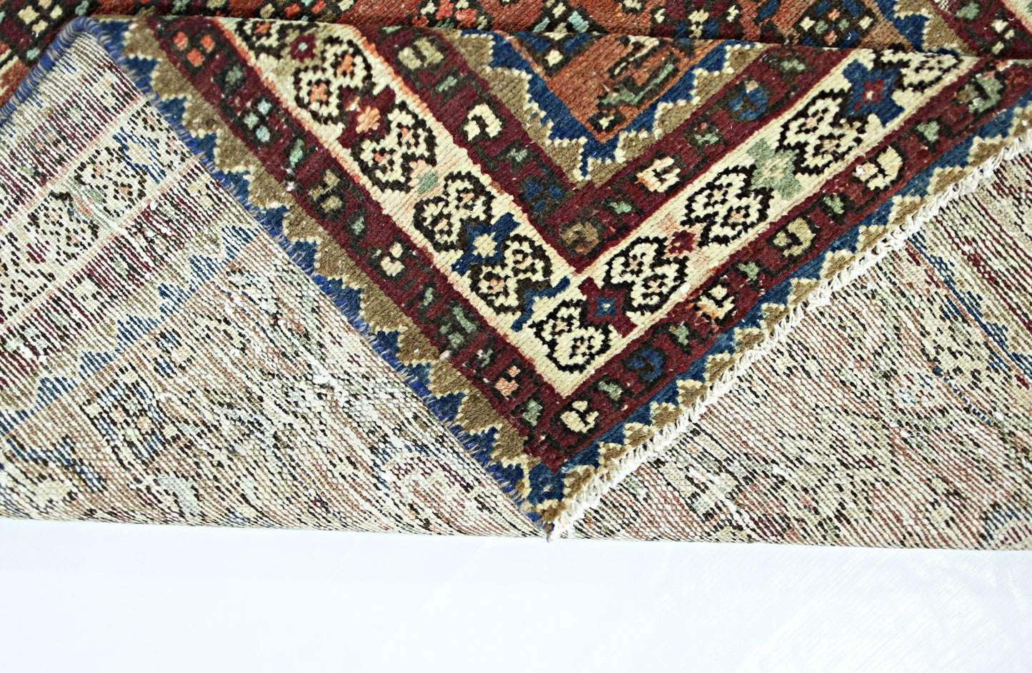 A folded vintage Persian runner featuring intricate geometric patterns in red, blue, and cream.