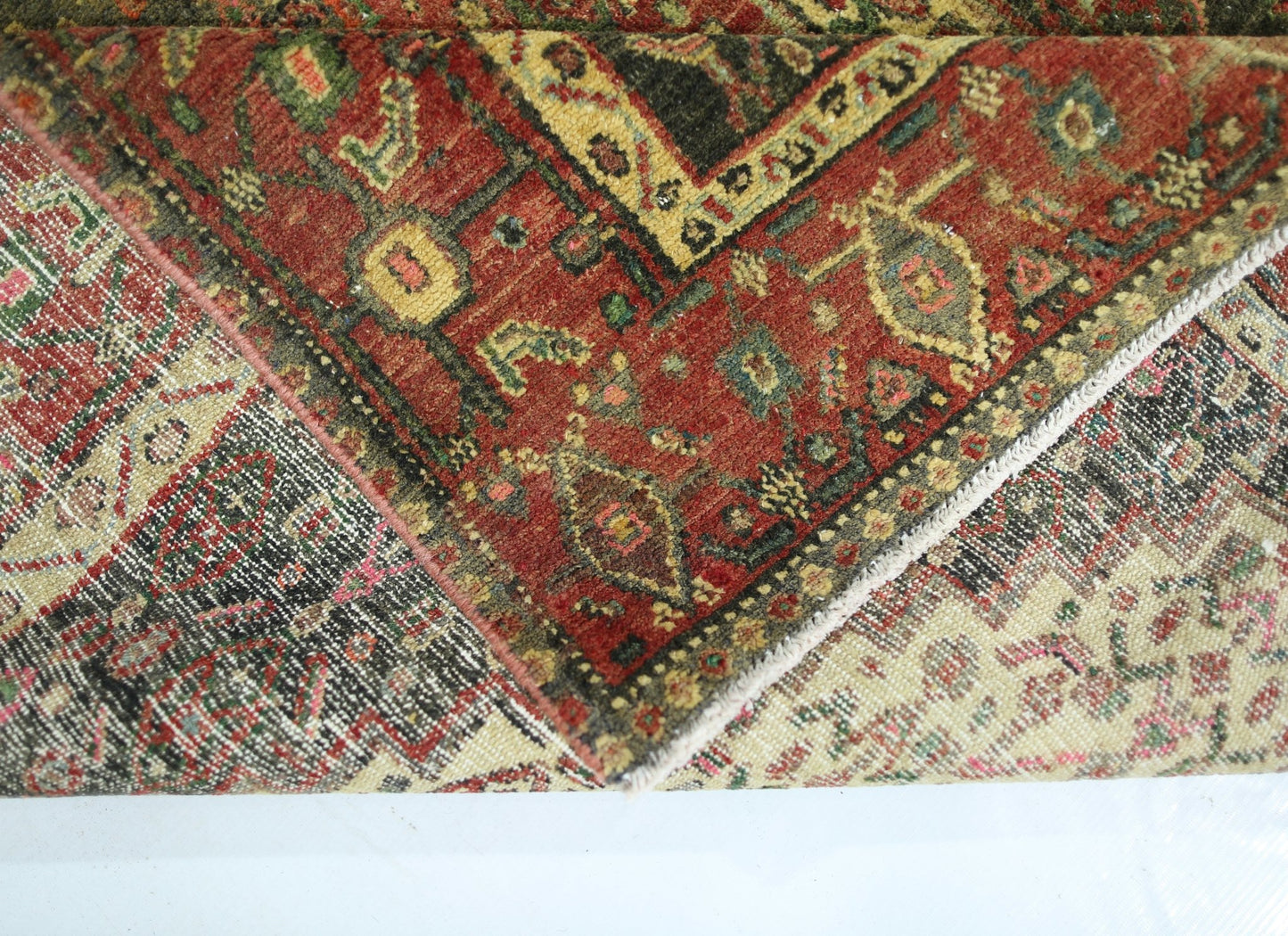 A folded vintage Persian Sanandaj rug featuring intricate red, green, and cream geometric patterns.
