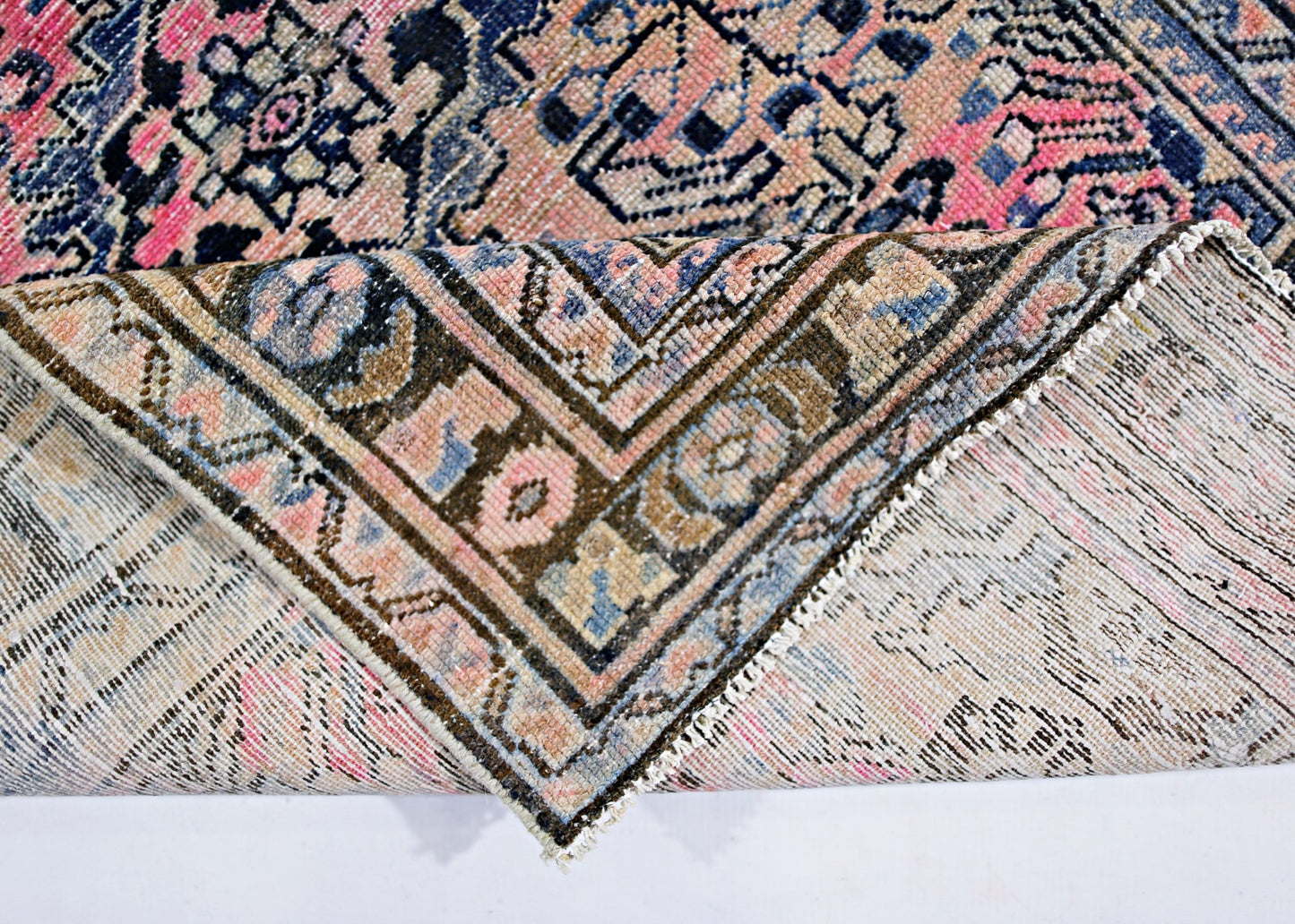 A vintage Persian rug with a folded corner revealing its intricate pink and blue floral pattern.