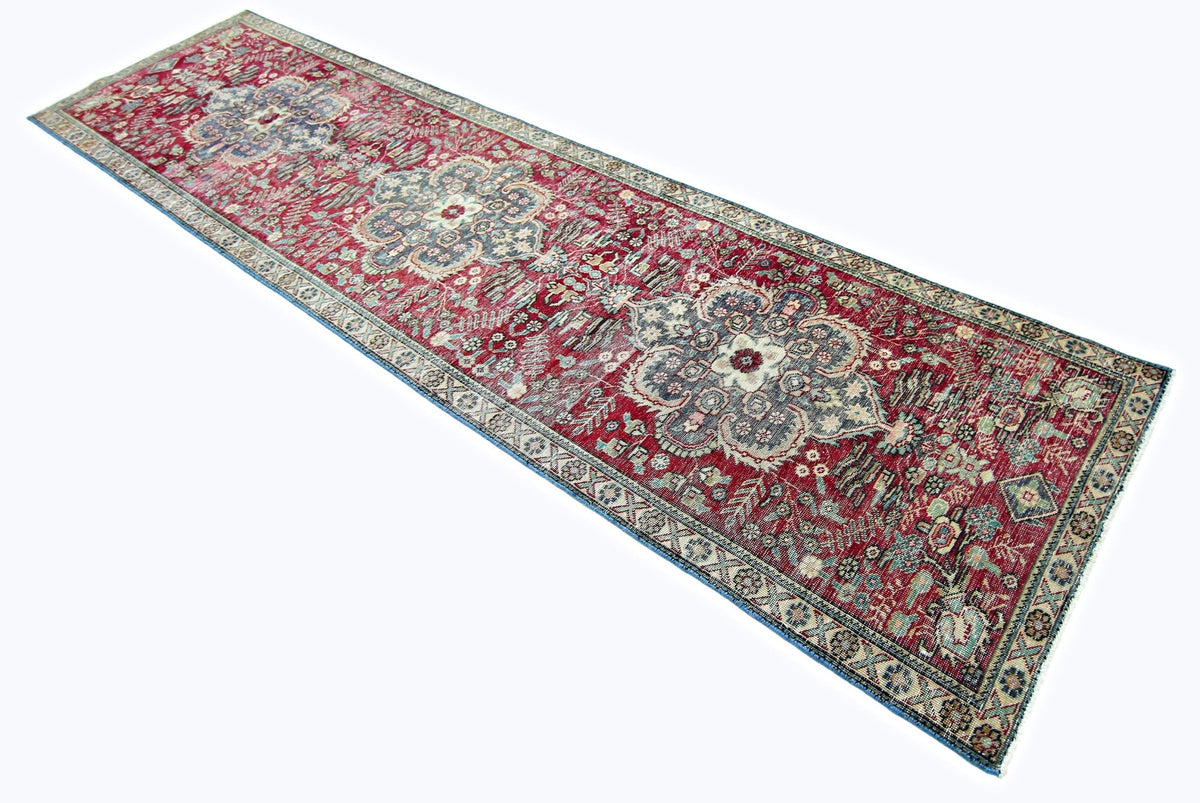 Vintage Persian Sarouk runner in red with intricate blue and cream floral patterns on a hand-knotted wool pile.