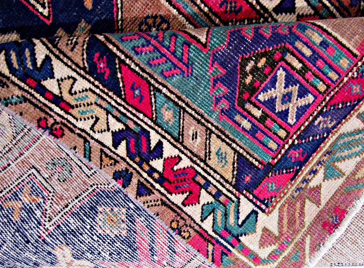 Close-up of a vintage Persian Saveh wool runner featuring intricate geometric floral patterns in navy, pink, and teal.