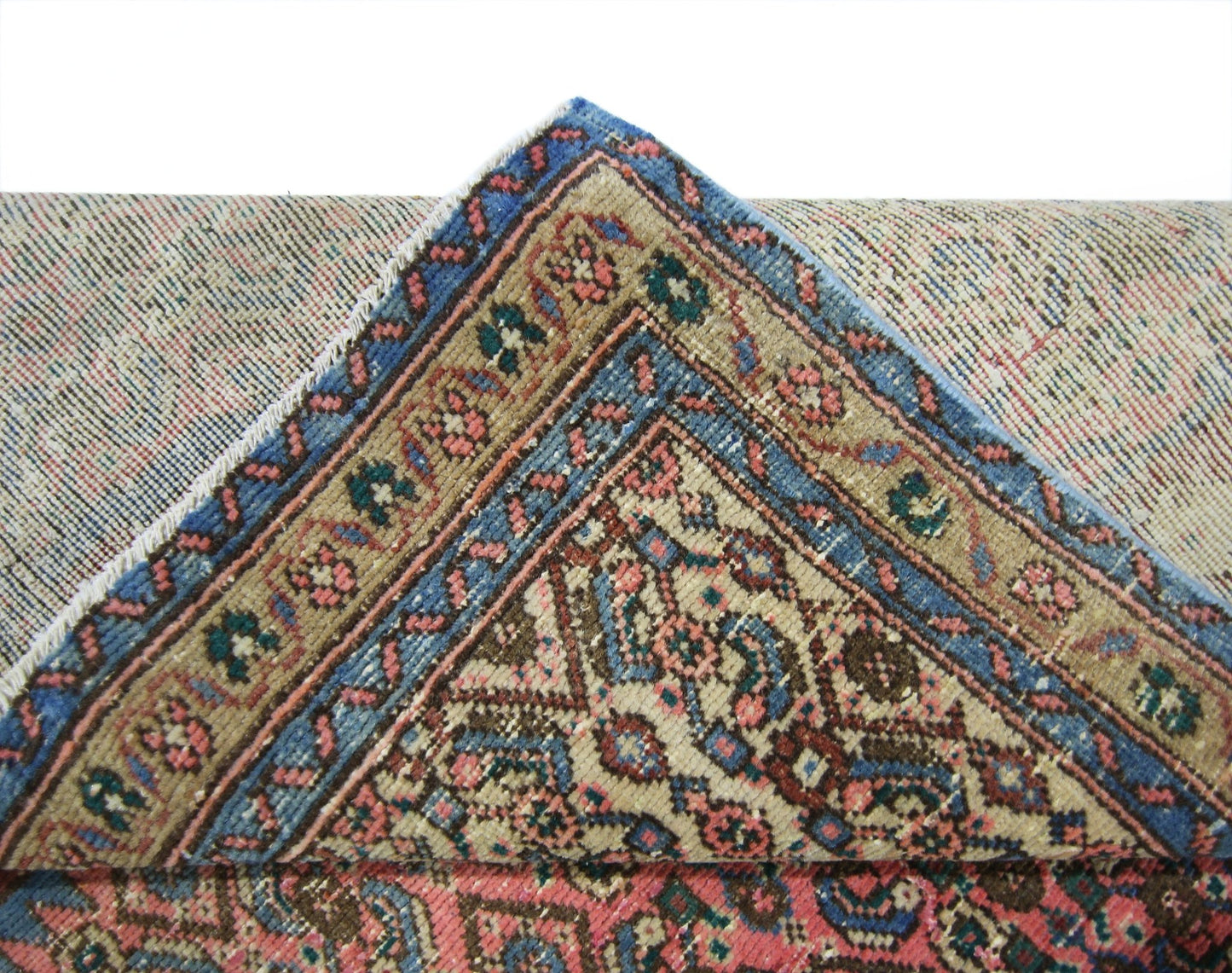 A corner of a vintage Persian Senneh runner folded back to reveal its intricate floral pattern.