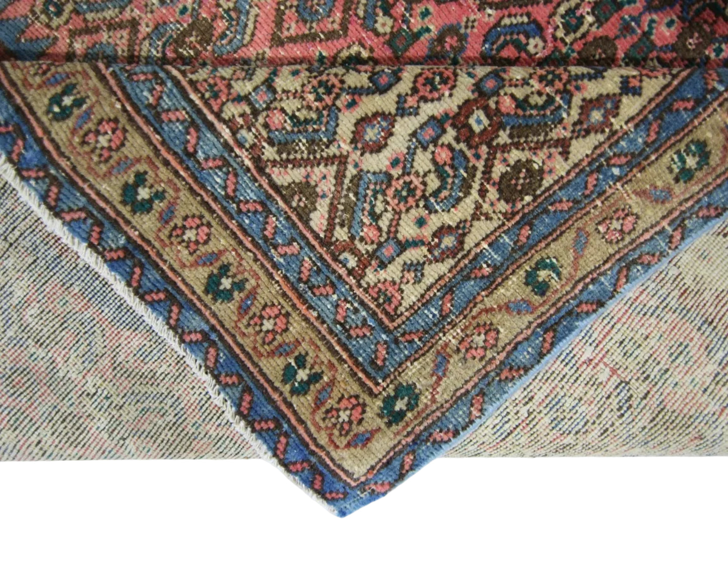 A corner of a vintage Persian Senneh runner folded back to reveal its intricate floral pattern.