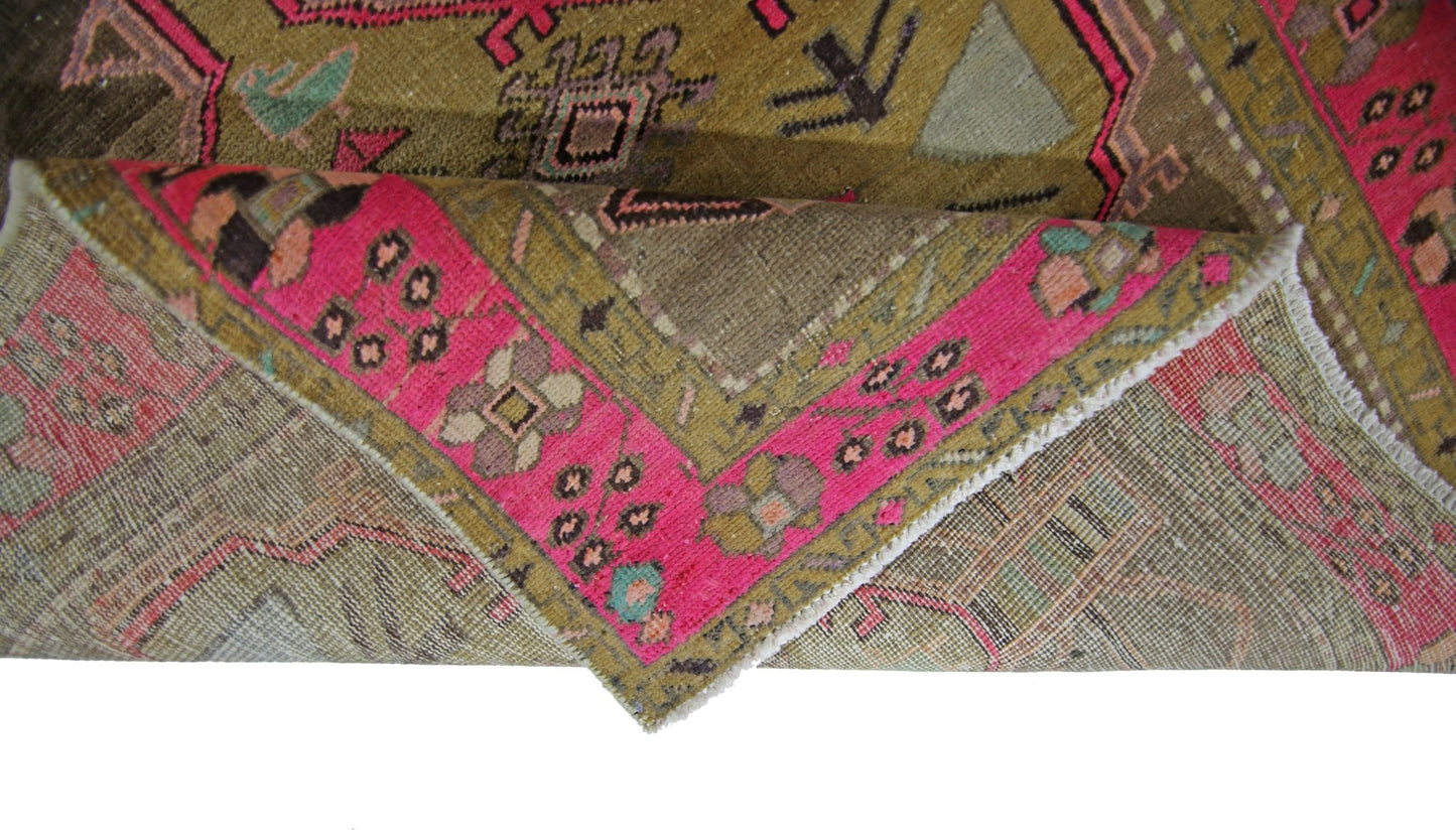 A folded vintage Persian Serab runner featuring geometric patterns in olive green and hot pink.