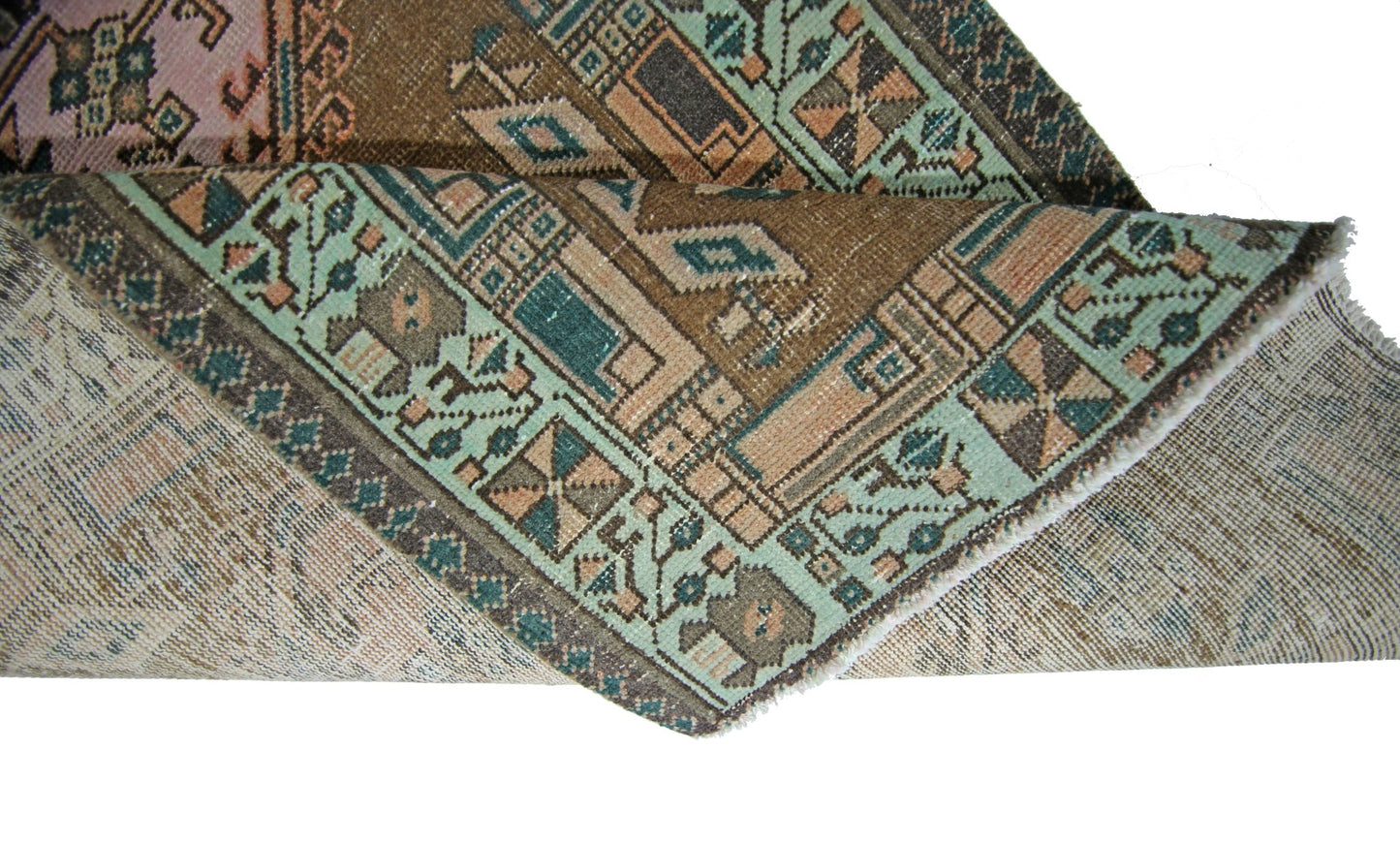 A folded vintage Persian Serab runner featuring geometric patterns in brown, teal, and pink.