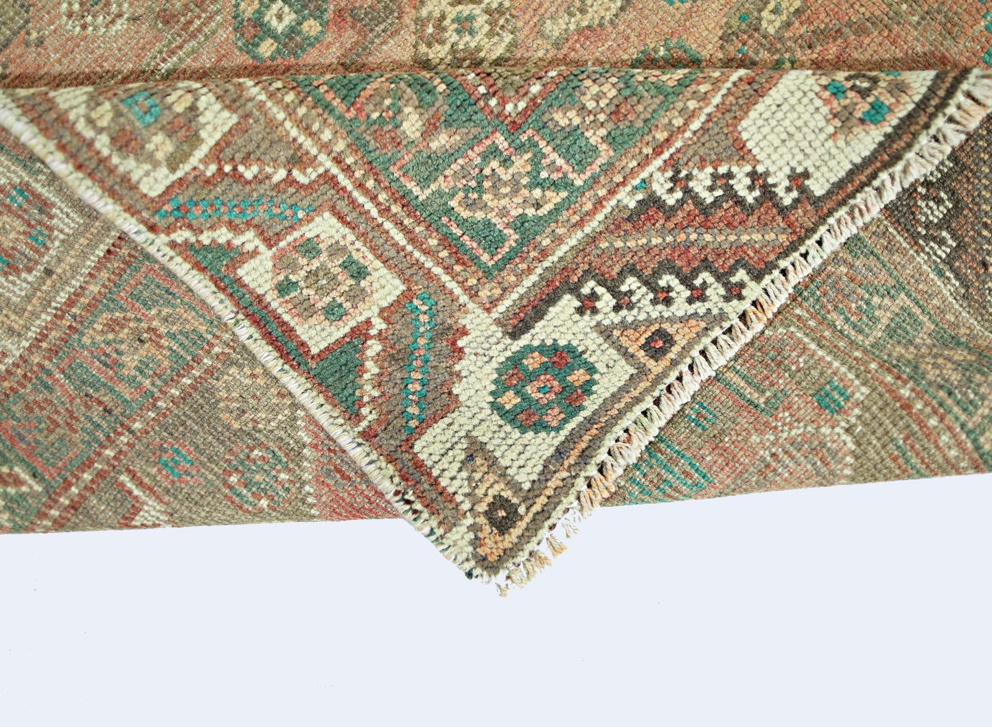 A folded vintage Persian Shiraz rug featuring intricate geometric patterns in muted earth tones.