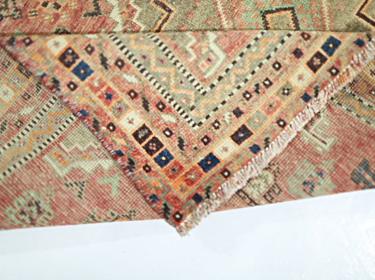A corner of a vintage Persian Shiraz rug is folded over to reveal its intricate geometric pattern.