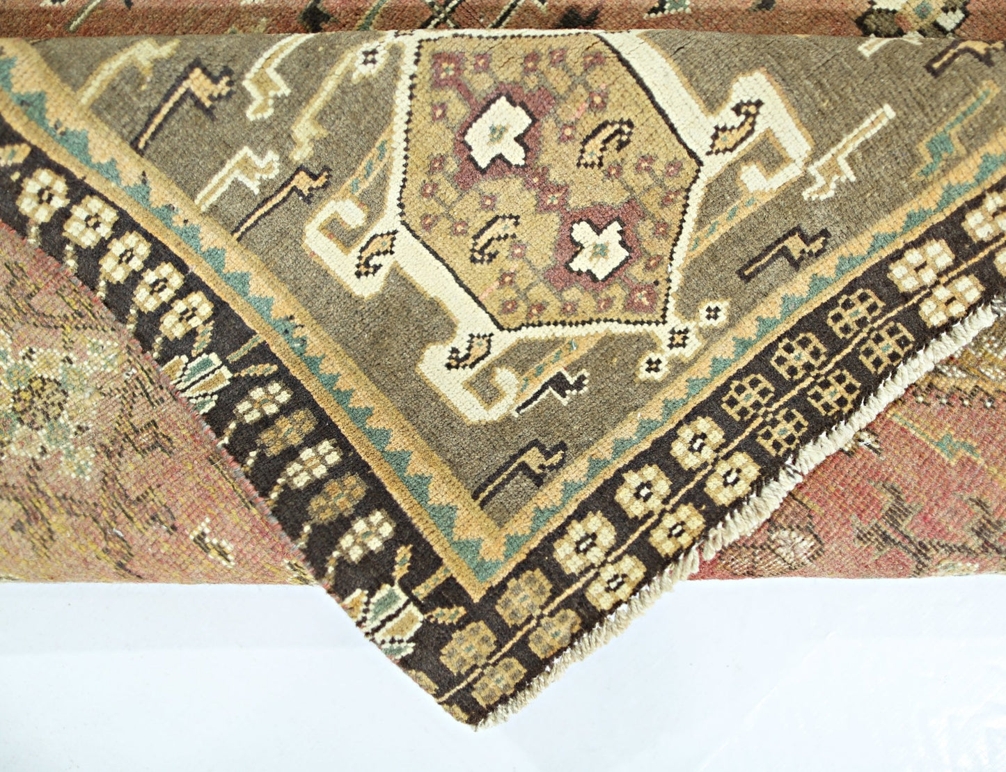 A folded vintage Persian Shiraz rug featuring a geometric medallion pattern in earthy tones.
