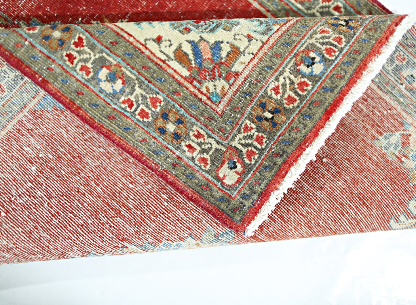 A folded vintage Persian Tabriz rug featuring intricate floral patterns in red, blue, and cream.