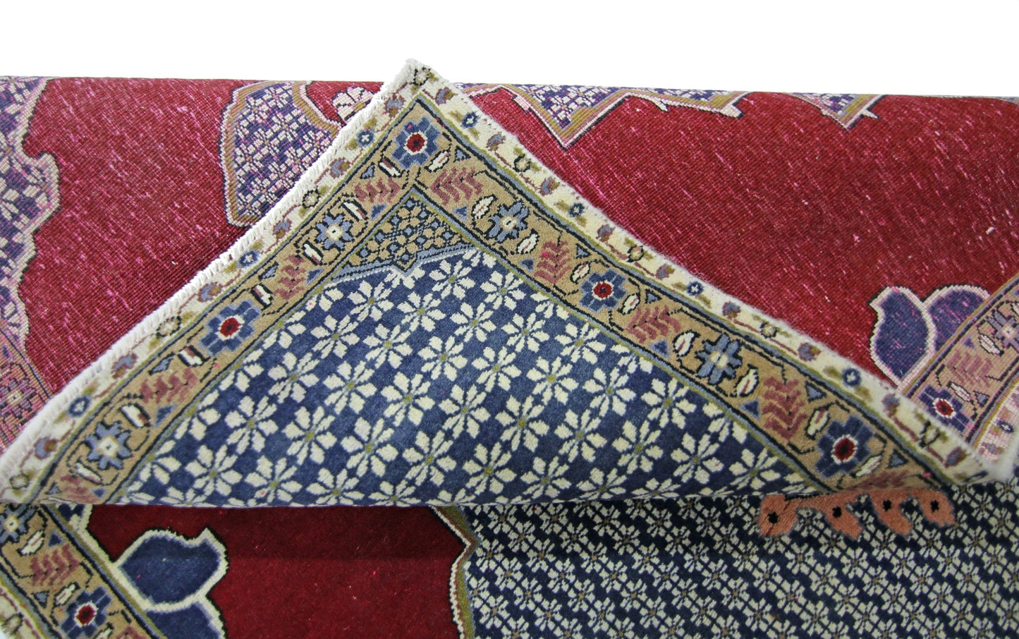 A folded vintage Persian rug featuring a red field with blue floral patterns and a detailed border.