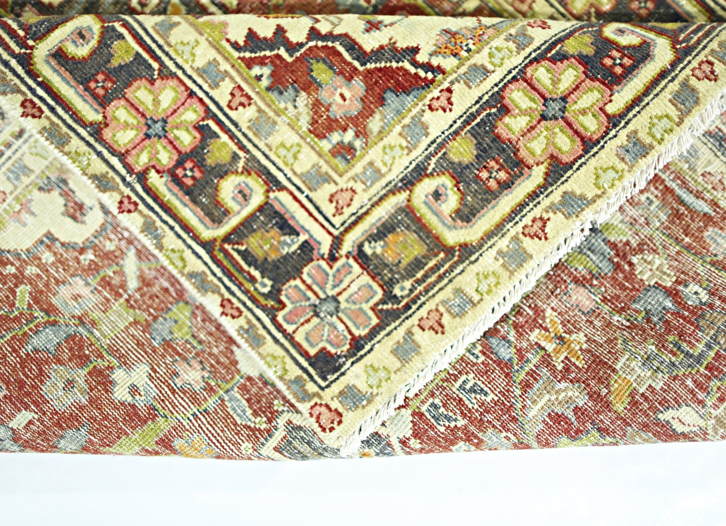 A folded vintage Persian rug featuring intricate floral patterns in red, blue, and cream tones.
