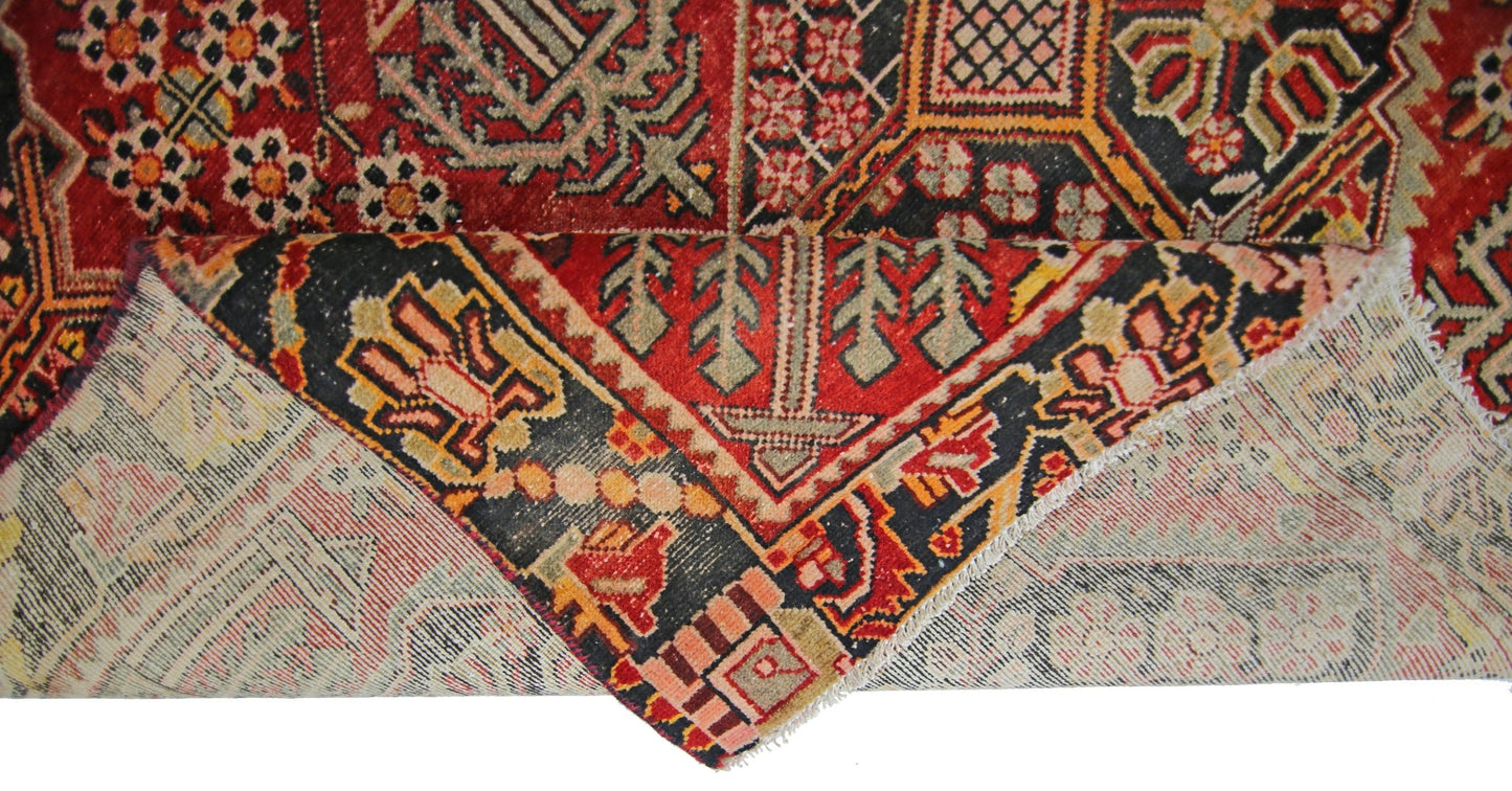 A vintage Persian Tabriz rug with a folded corner showing its intricate red and black pattern.