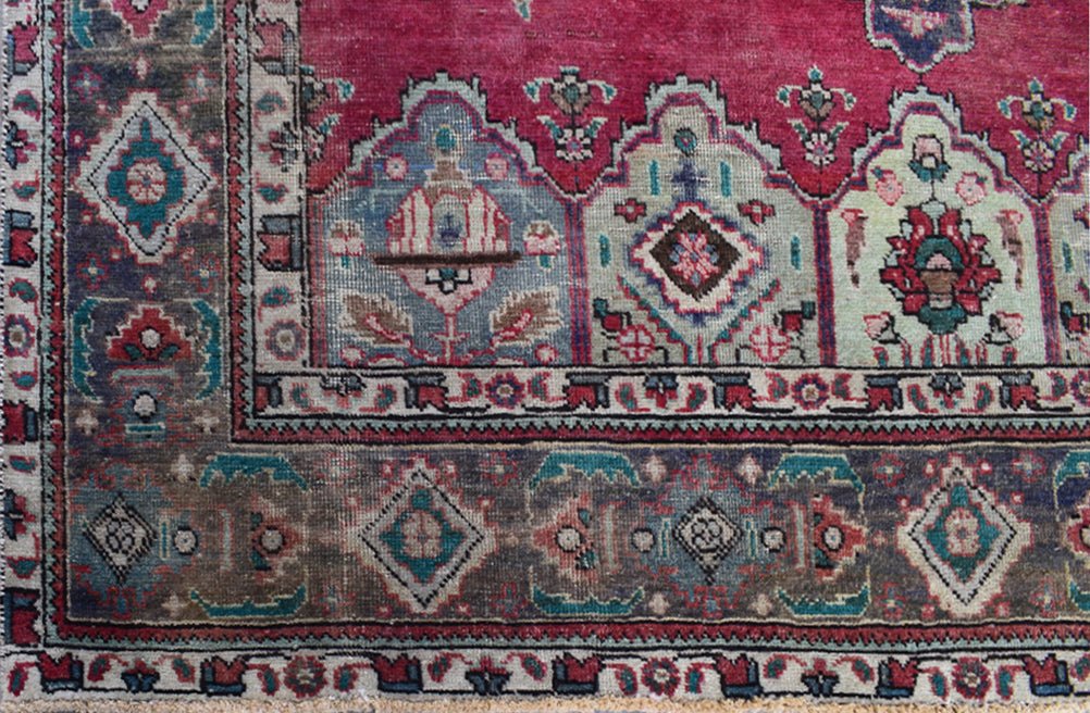 A vintage Persian Tabriz rug featuring a deep red field with intricate floral and medallion motifs.