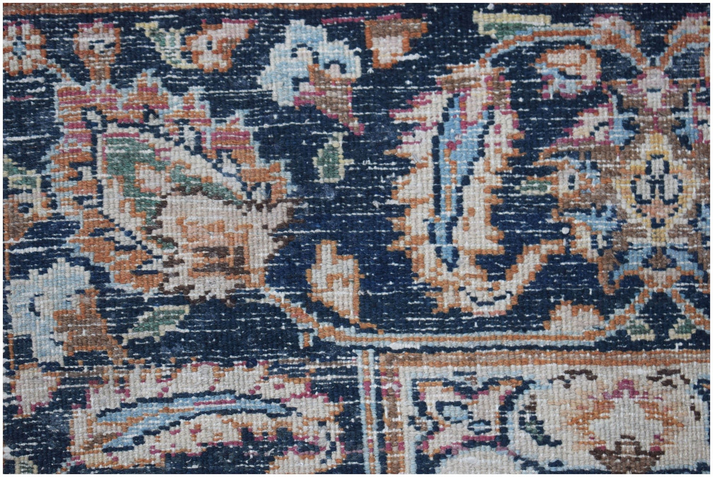 A close-up of a vintage Persian Kerman rug featuring intricate floral patterns on a dark blue field.
