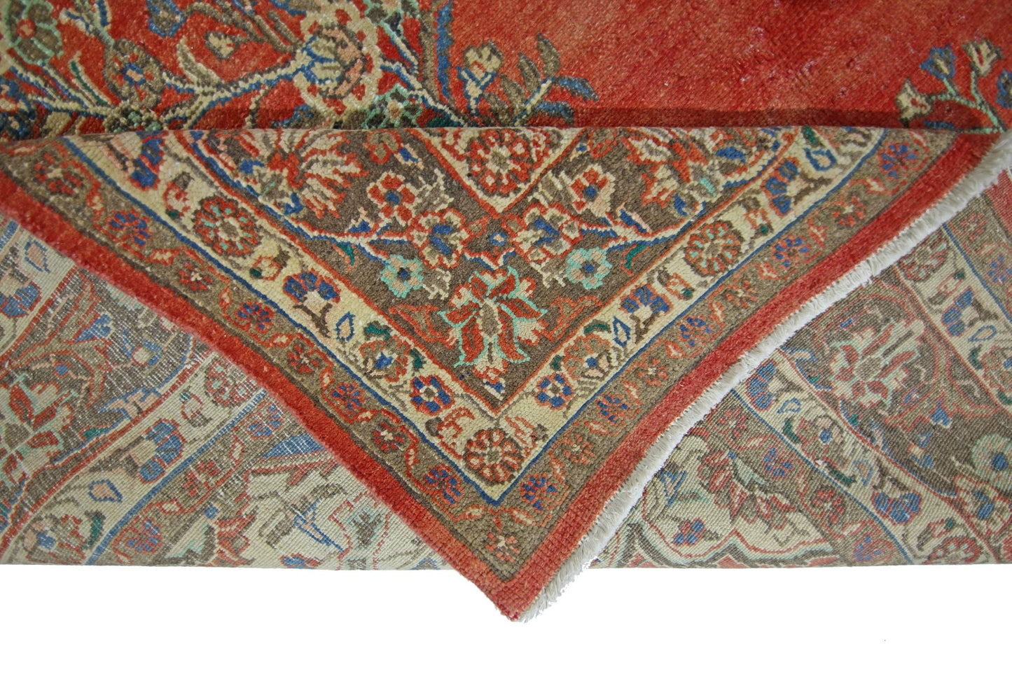 A corner of a vintage Persian Tabriz rug is folded back to reveal its intricate floral pattern.
