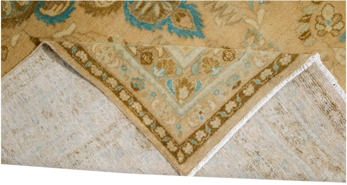 A vintage Persian Tabriz rug with a tan and blue floral pattern, shown folded to reveal its back.