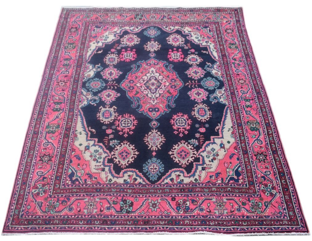 A vintage Persian Tabriz rug featuring a central pink medallion on a dark blue field.