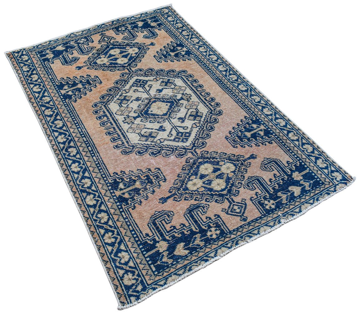 A vintage handwoven Persian rug featuring blue geometric patterns on a faded peach background.