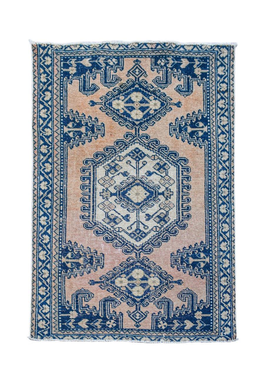 A vintage handwoven Persian rug featuring a blue geometric medallion on a faded peach background.