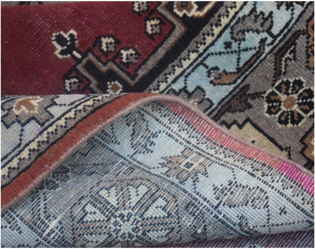 A close-up of a vintage handmade Persian wool rug showing its intricate floral pattern and backing.