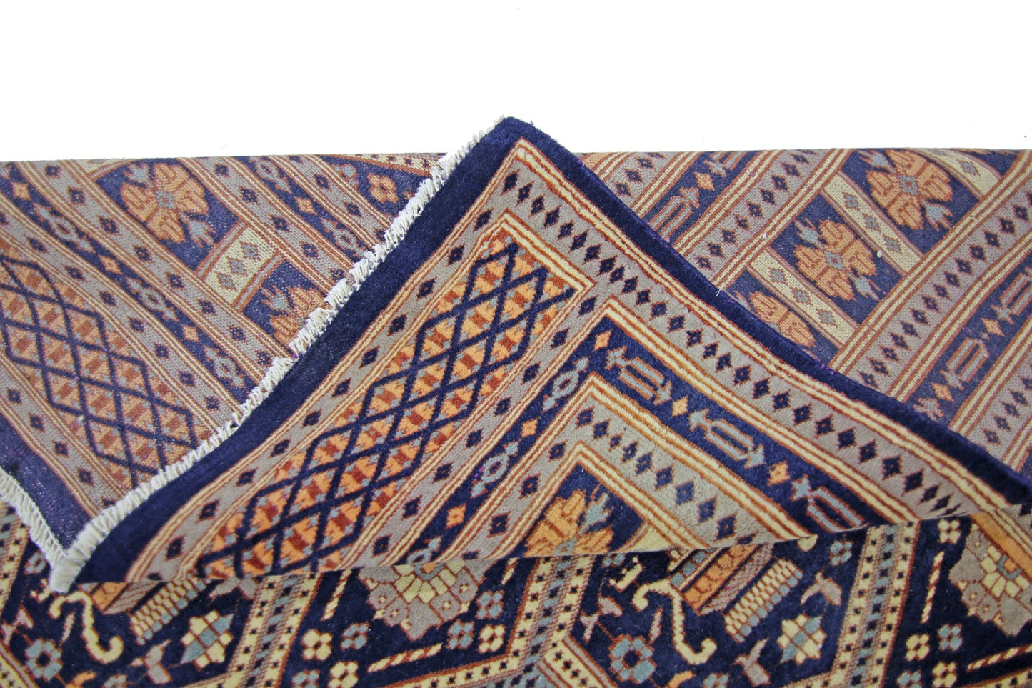 A vintage Pakistani Princess Bokhara rug with a folded corner showing its intricate geometric pattern.