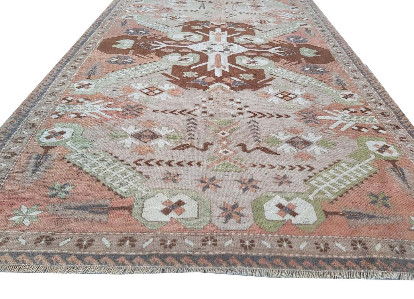 A vintage handmade Turkish rug featuring geometric patterns in shades of brown, green, and pink.