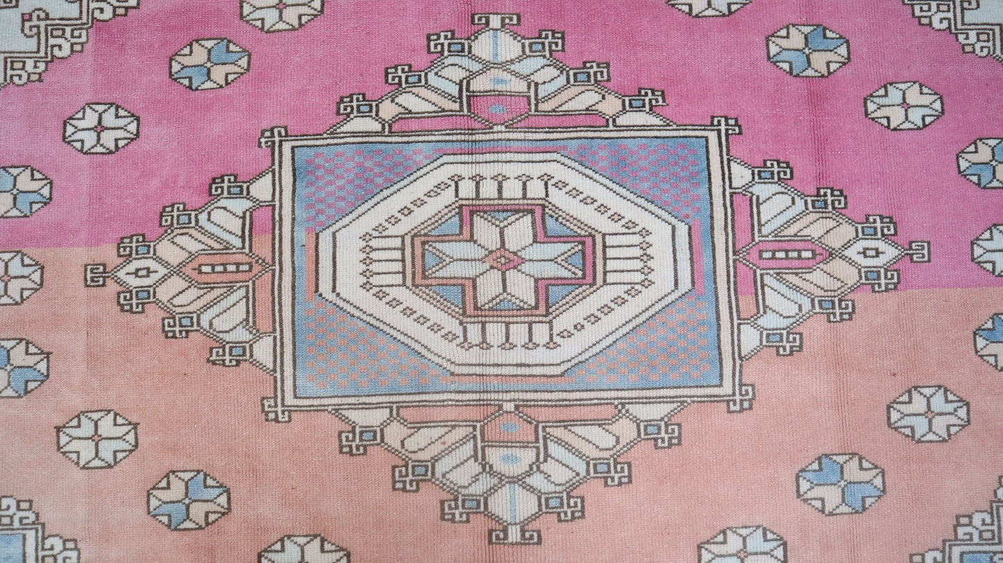 A vintage Turkish Anatolian rug featuring a geometric tribal pattern in pink and blue tones.