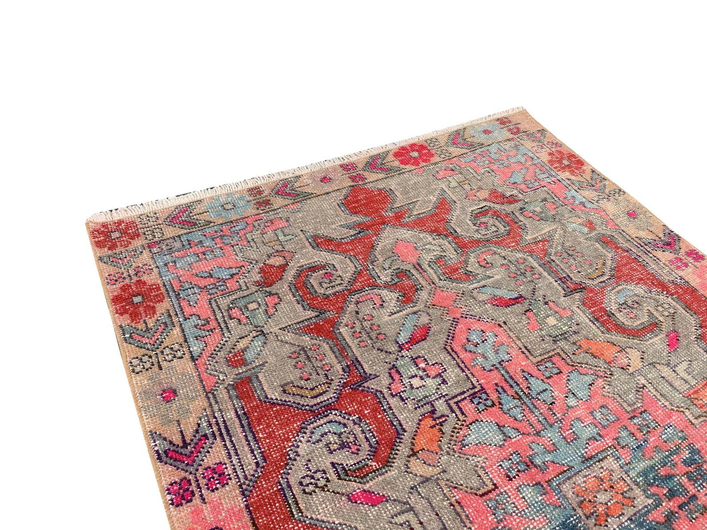A handmade vintage Turkish rug featuring a geometric floral pattern in red, pink, and grey tones.