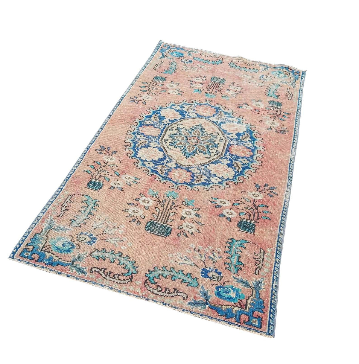 A handmade vintage Turkish rug featuring a central blue floral medallion on a faded pink background.