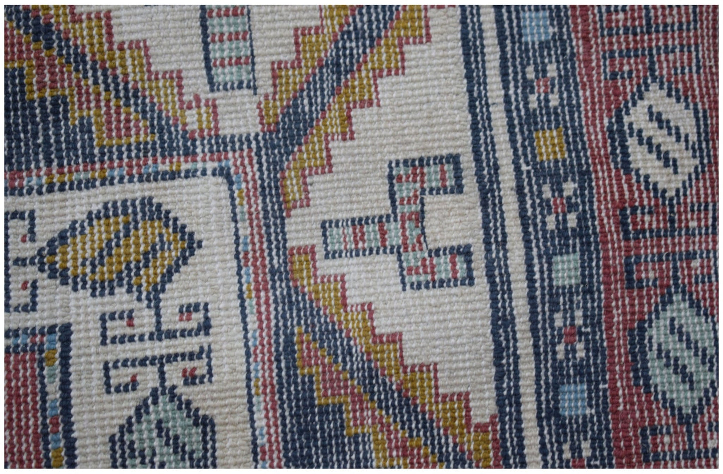 A close-up of a vintage handwoven Turkish rug featuring geometric patterns in red, blue, and gold.