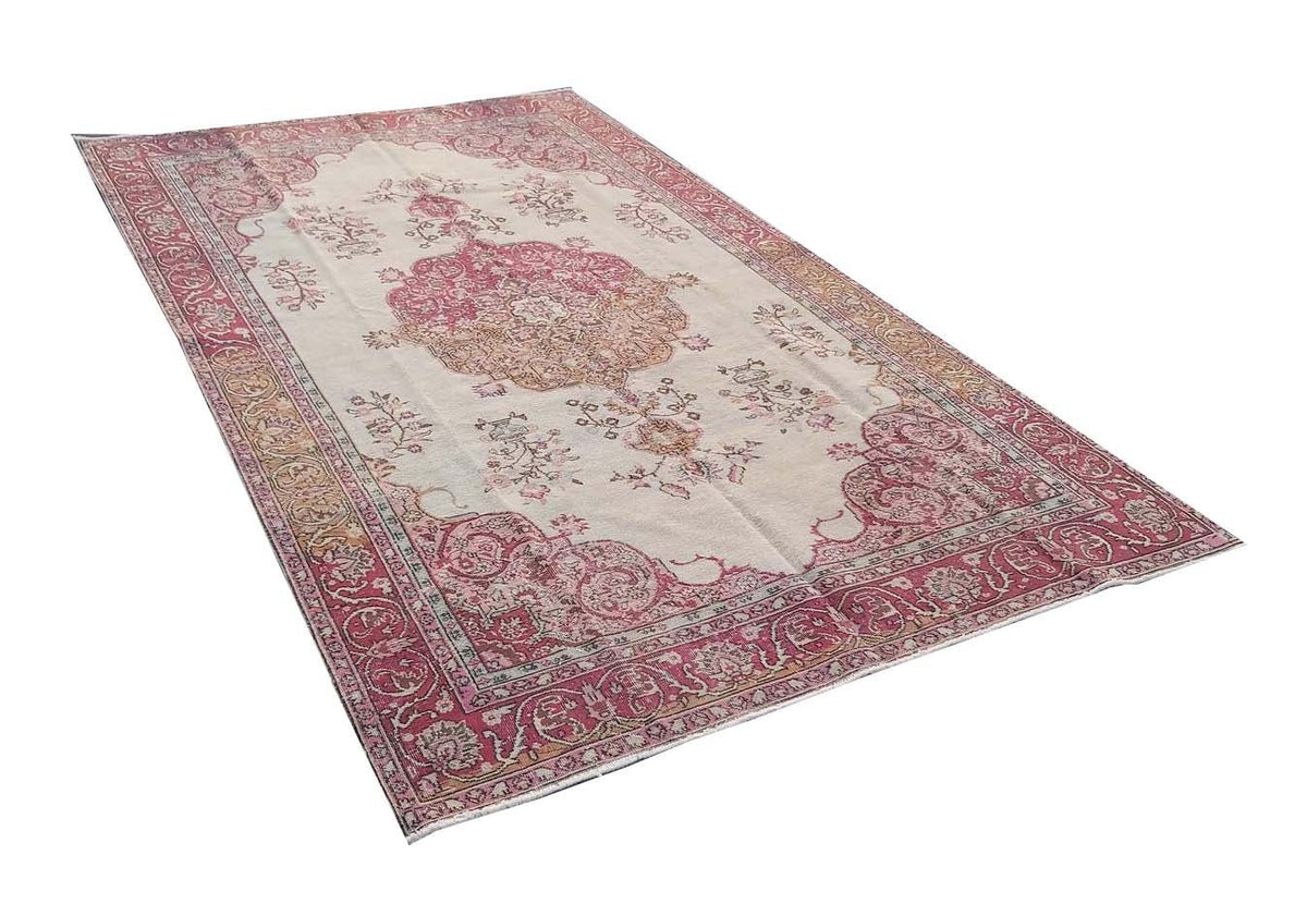 A vintage handmade Turkish wool rug featuring a central floral medallion in pink and cream tones.