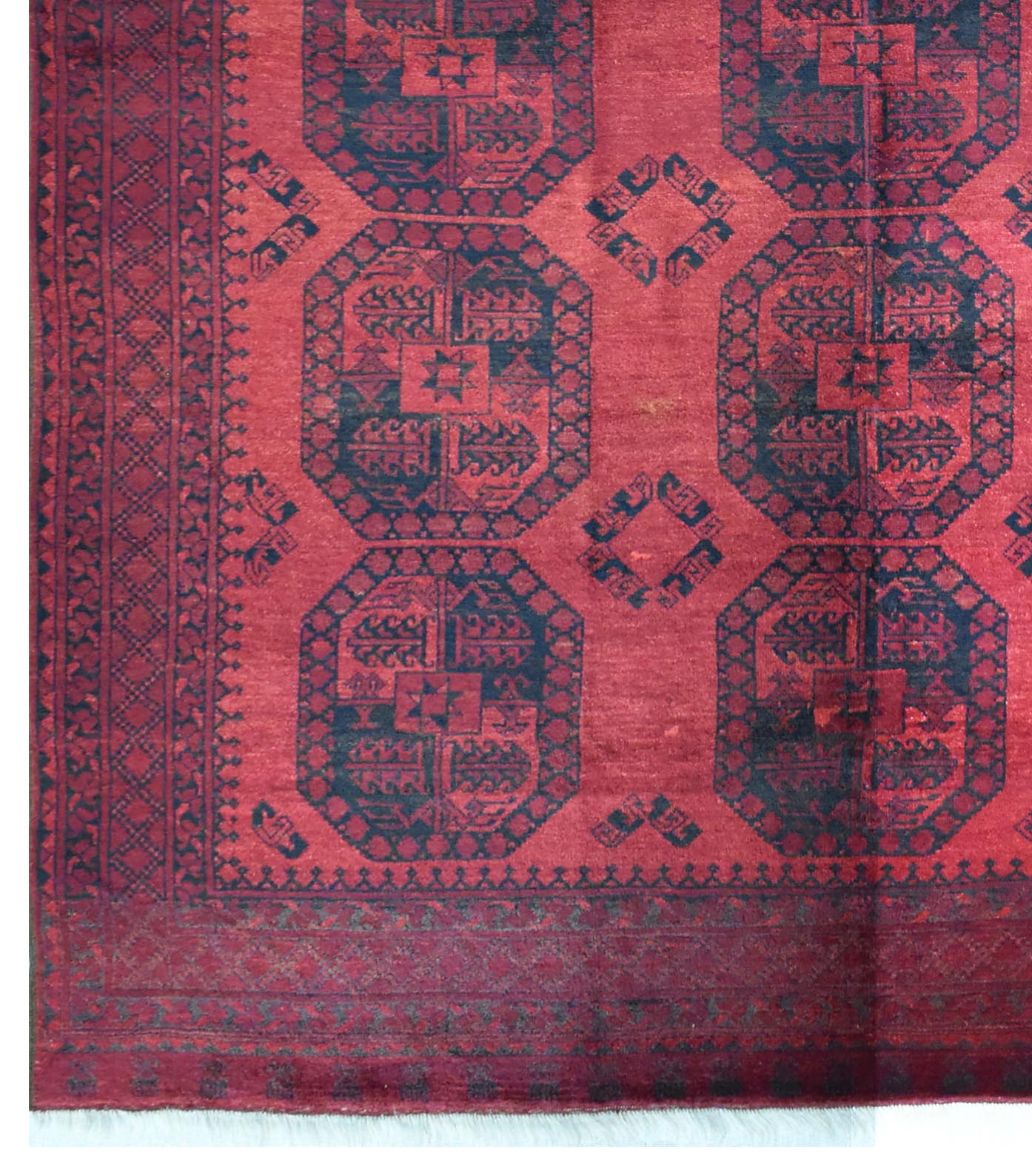 A vintage Afghan Turkmen rug featuring repeating dark blue octagonal motifs on a red wool field.