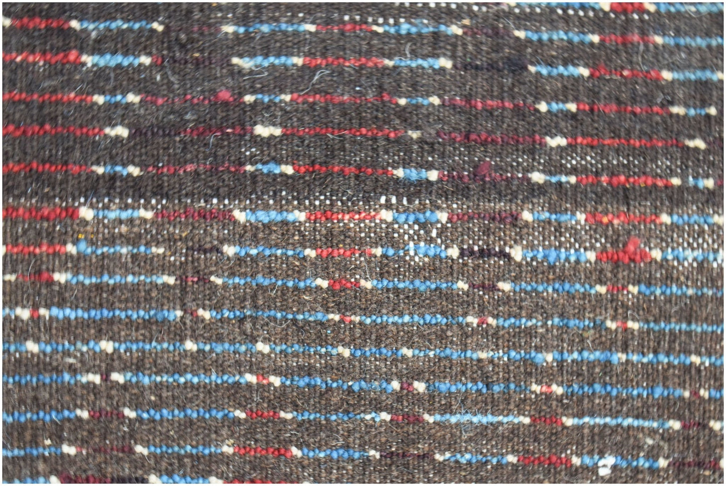 A close-up of a hand-knotted Afghan rug featuring horizontal stripes in blue, red, and cream.