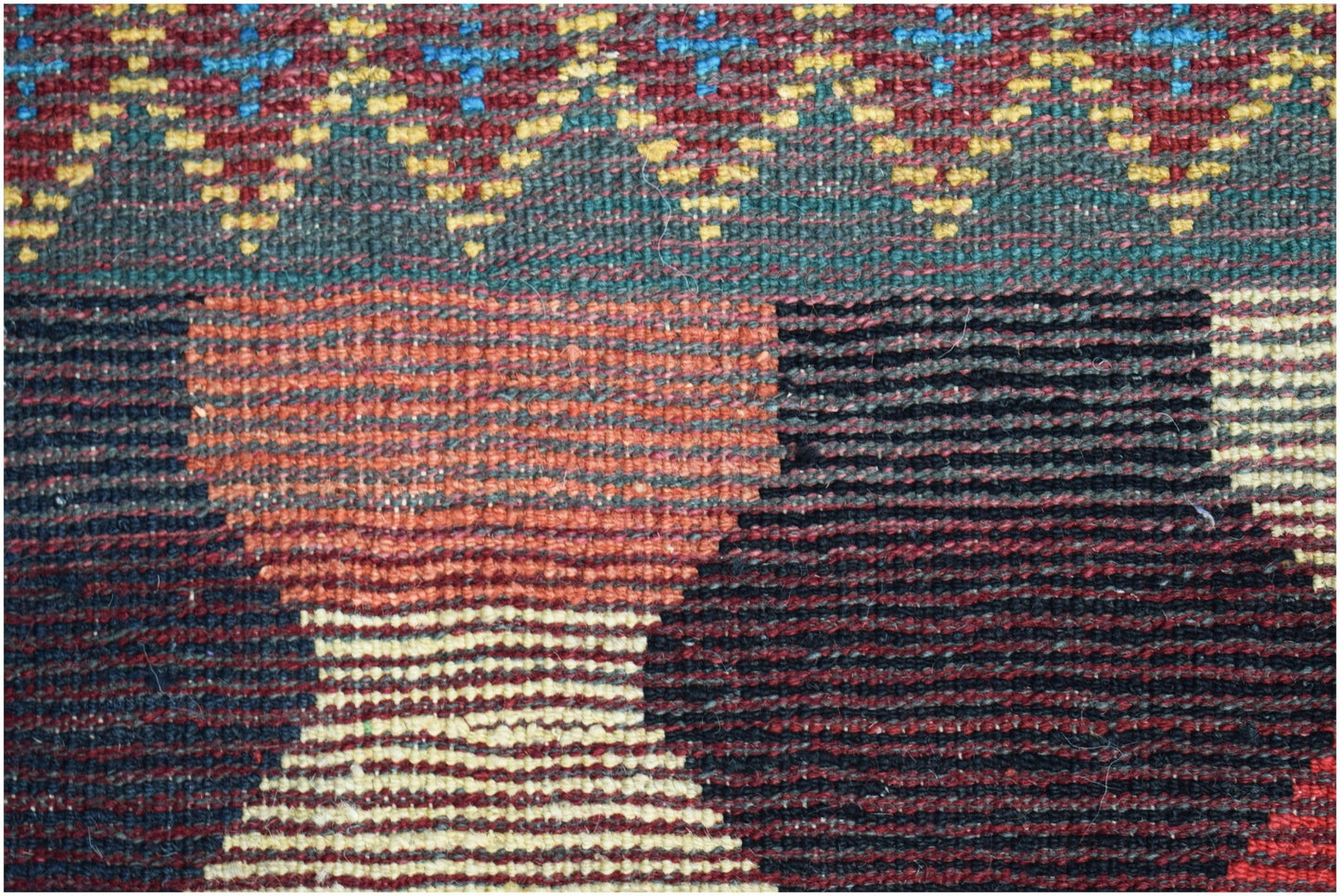 A close-up of a hand-knotted Afghan wool rug featuring geometric patterns in red, black, and yellow.