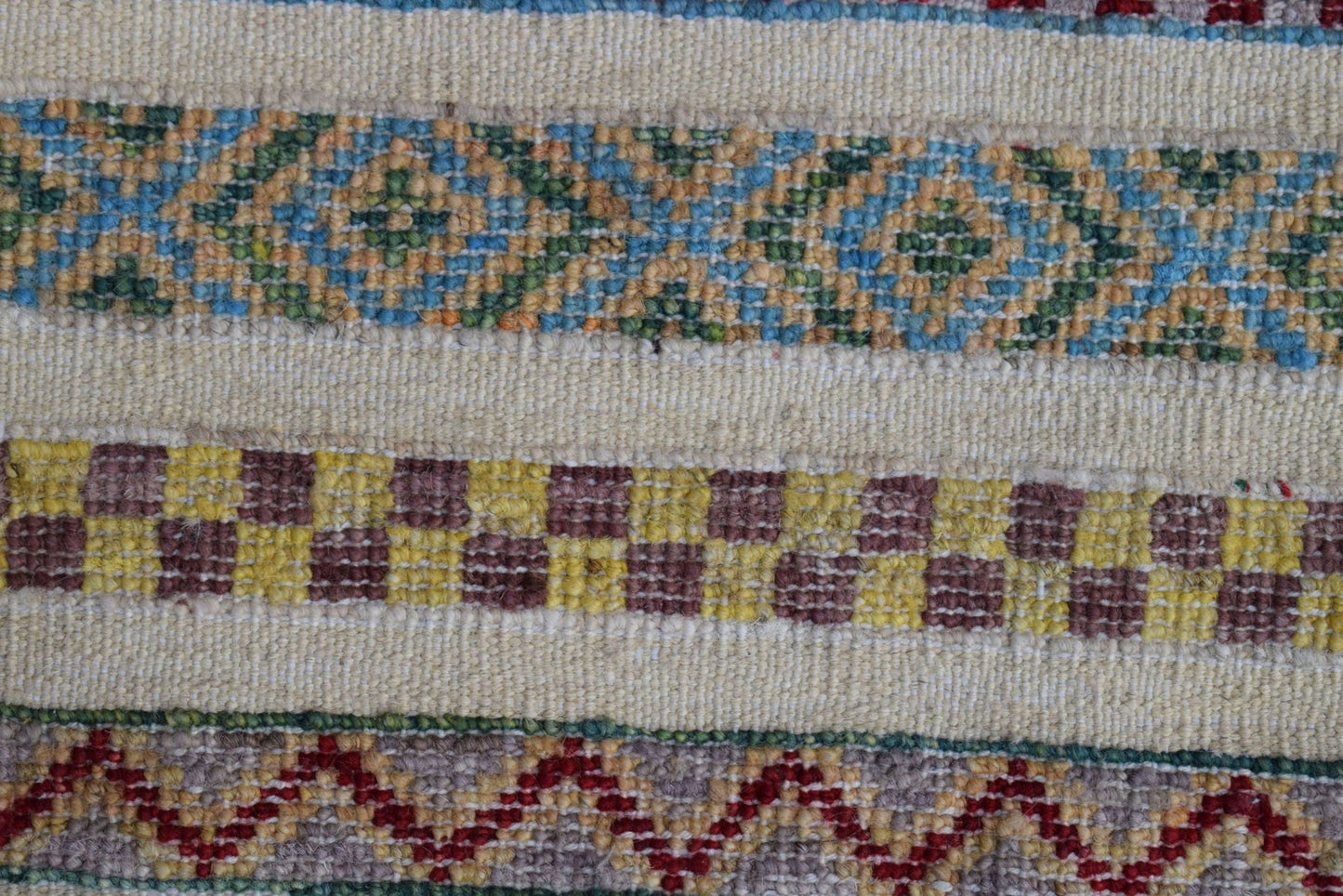 A close-up of an Afghan Yekta rug featuring horizontal bands of geometric, checkered, and zigzag patterns.