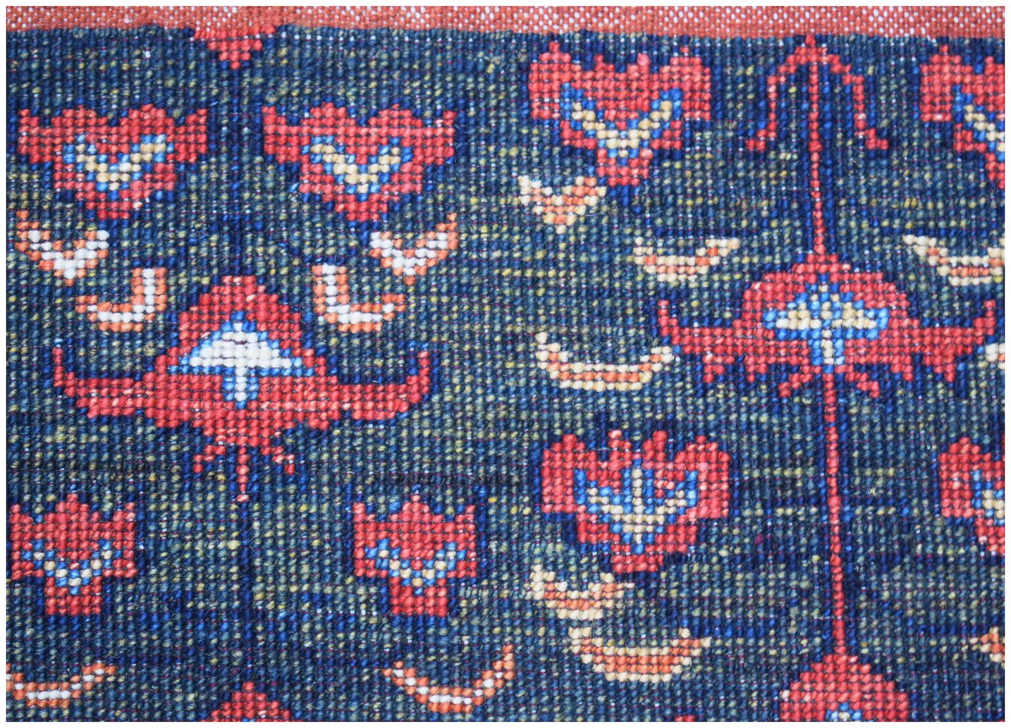 A close-up of a handmade Afghan Chobi rug featuring traditional red and blue floral motifs.