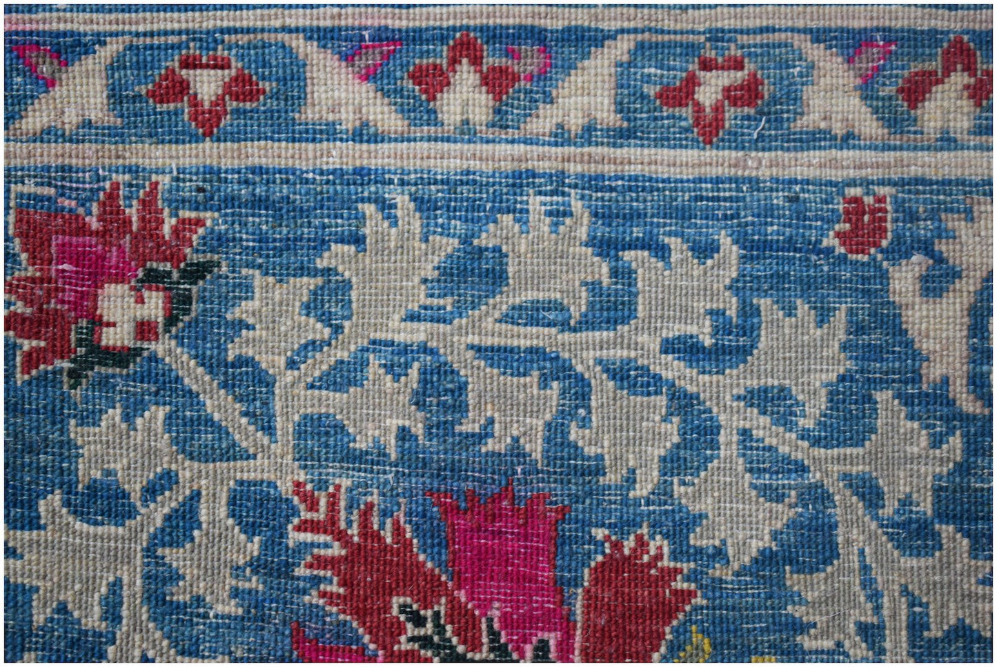 A close-up of an Afghan Chobi rug featuring intricate floral patterns in red, blue, and cream.