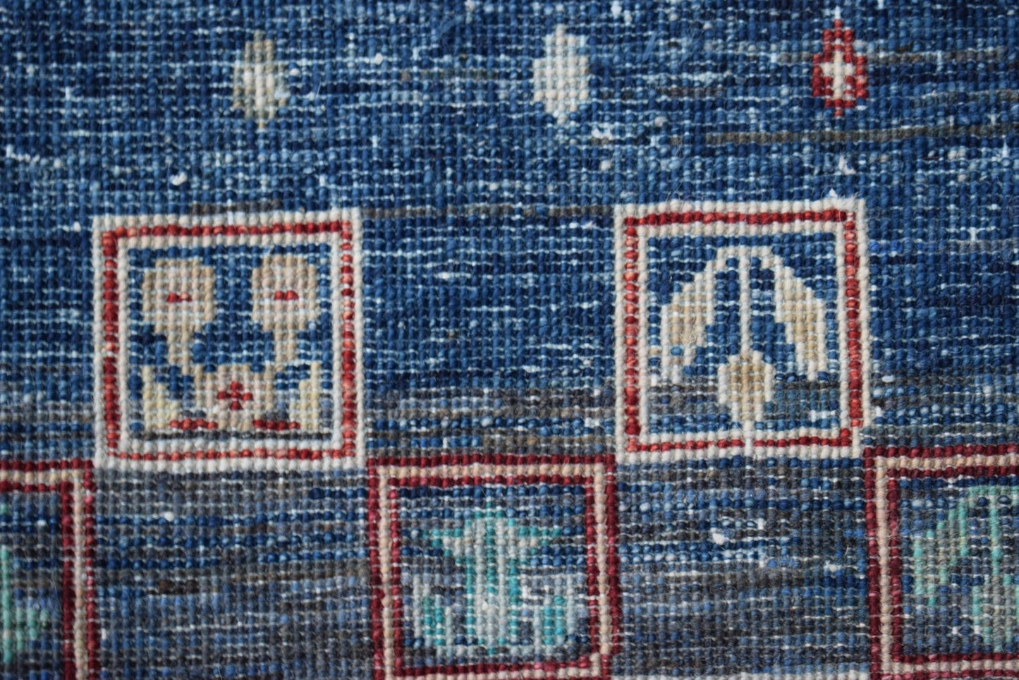 A close-up of a handmade Afghan Chobi rug featuring geometric motifs in red and blue squares.