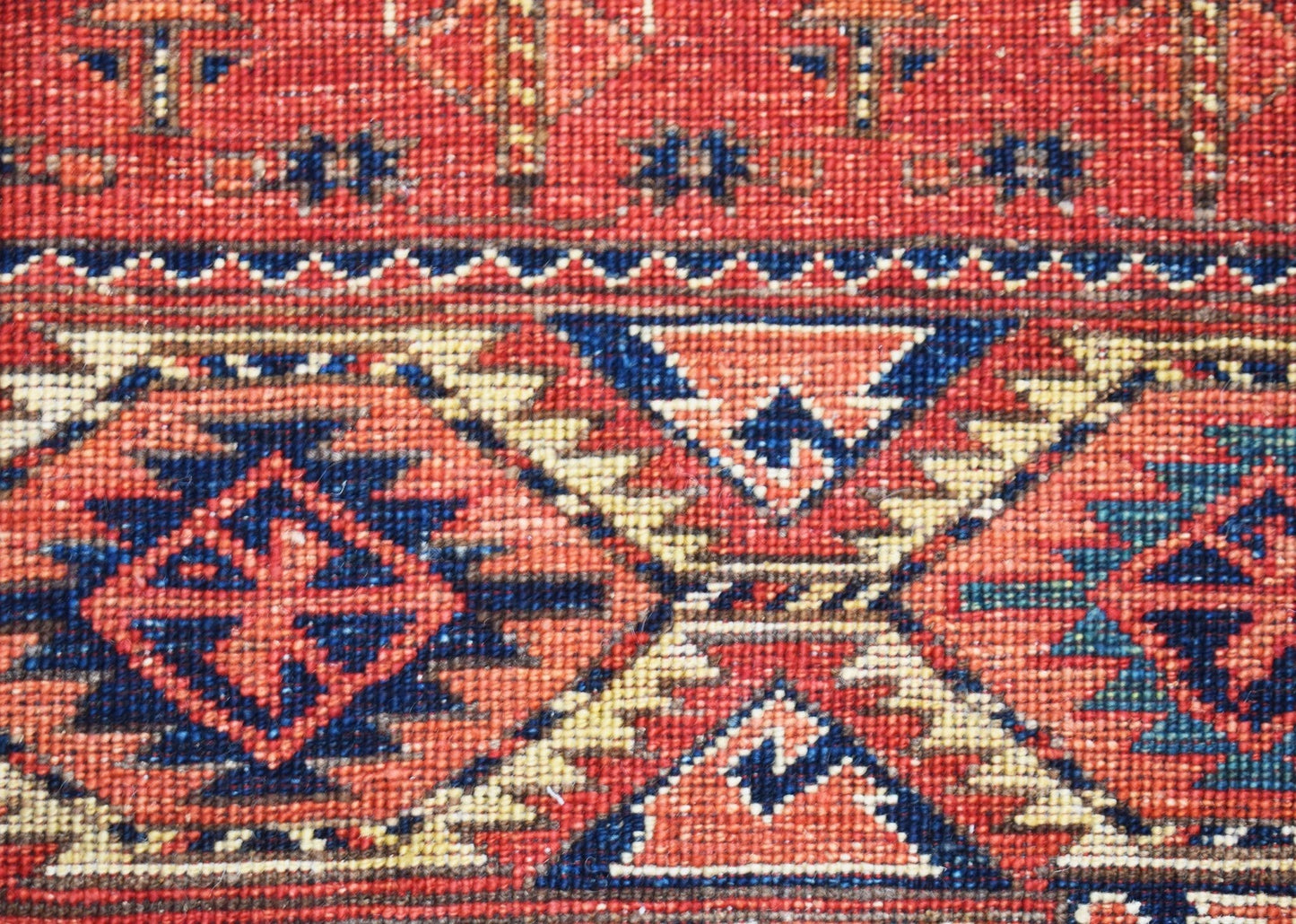 A close-up of a handwoven Afghan Chobi rug featuring traditional geometric patterns in red and blue.