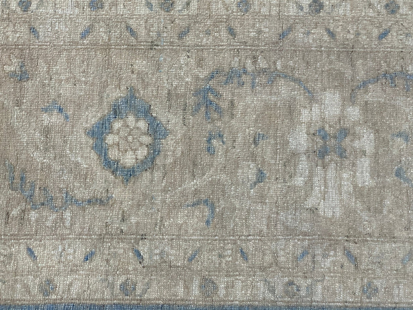 A handmade Afghan Chobi rug featuring a traditional floral pattern in muted blue and beige tones.