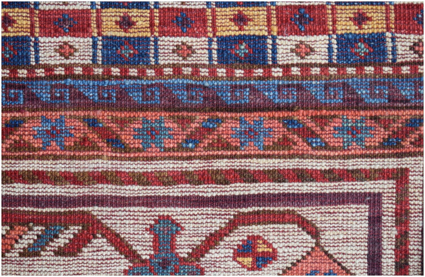 A close-up of an Afghan Herati rug featuring intricate geometric patterns in red, blue, and cream.