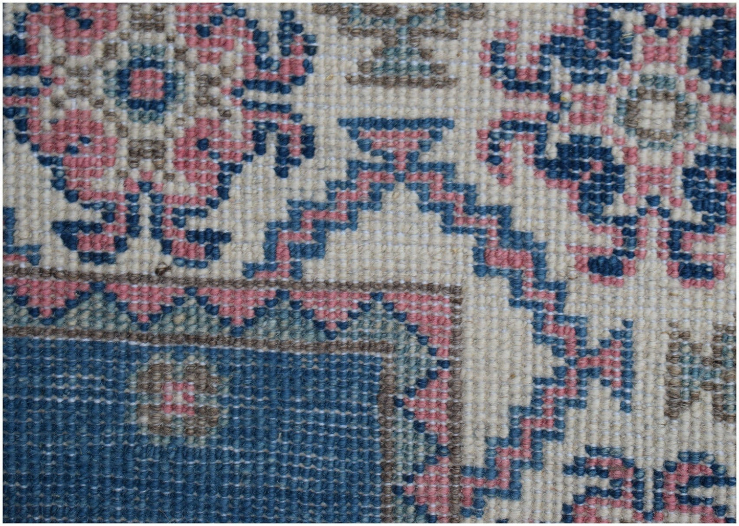 A close-up of an Afghan Kazakh runner featuring traditional geometric motifs in blue and pink wool.