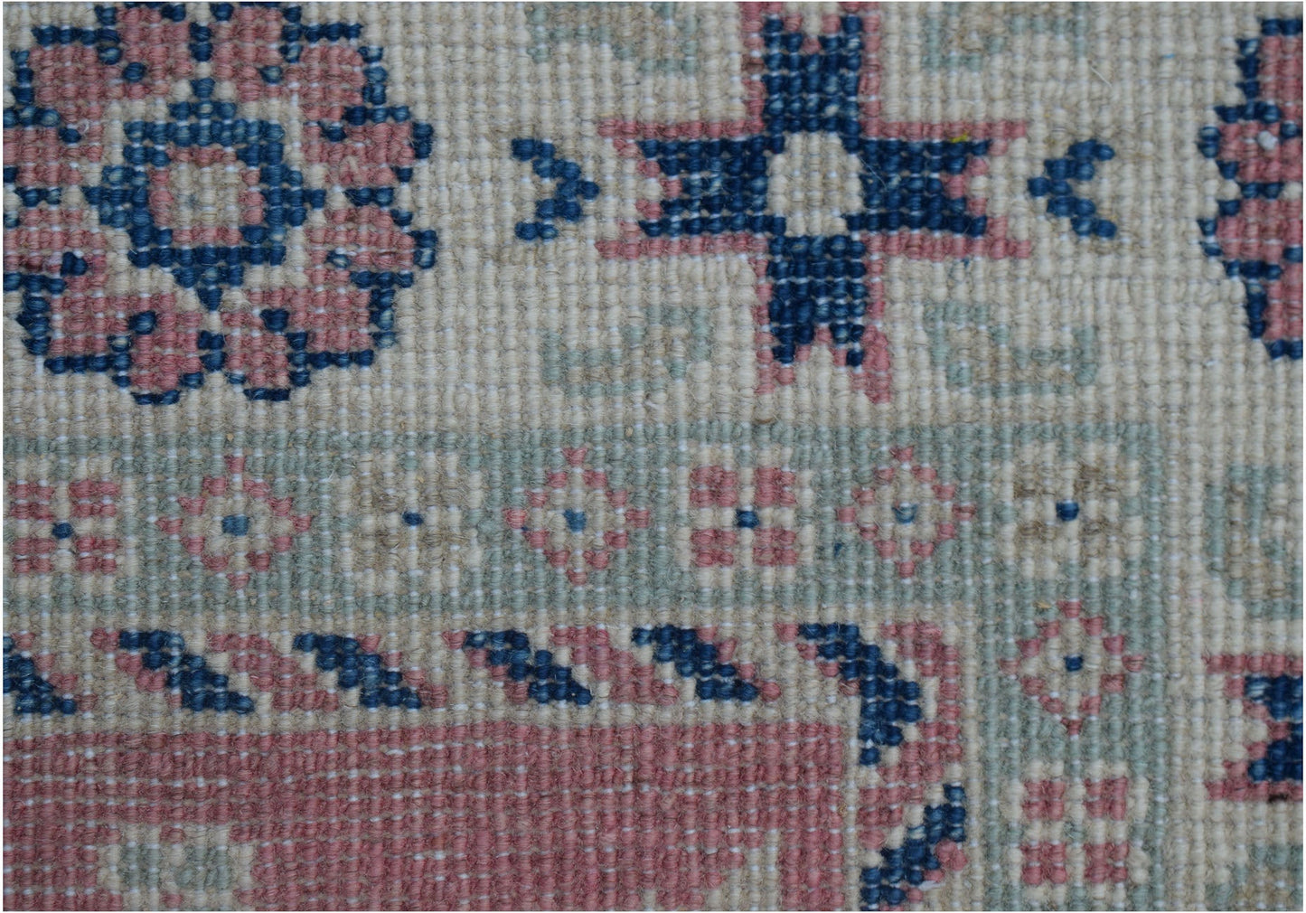 A close-up of an Afghan Kazakh runner featuring traditional geometric motifs in blue and pink wool.